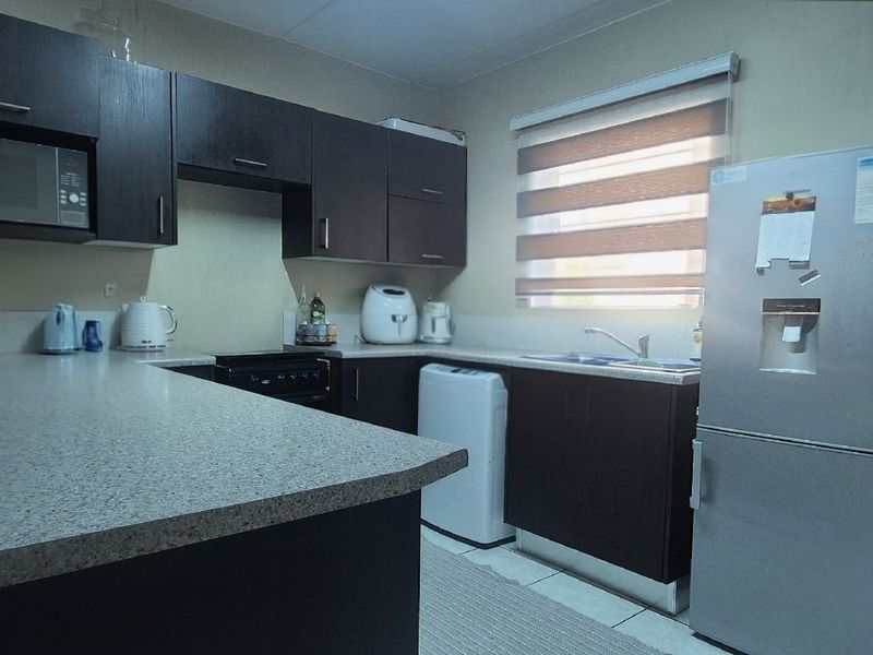 A functional kitchen featuring dark wood cabinetry, ample laminate counter space, a stainless steel sink, and integrated microwave, offering a practical layout for daily use.