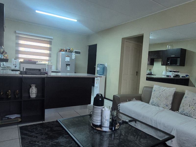 Open-plan living area featuring a kitchen with dark cabinetry, tiled flooring, and a large wall-mounted mirror, creating a functional combined living and cooking space.