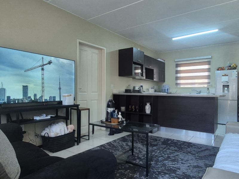 Open-plan living area featuring a functional kitchen with dark cabinetry, a breakfast island, and tiled flooring throughout the combined space.