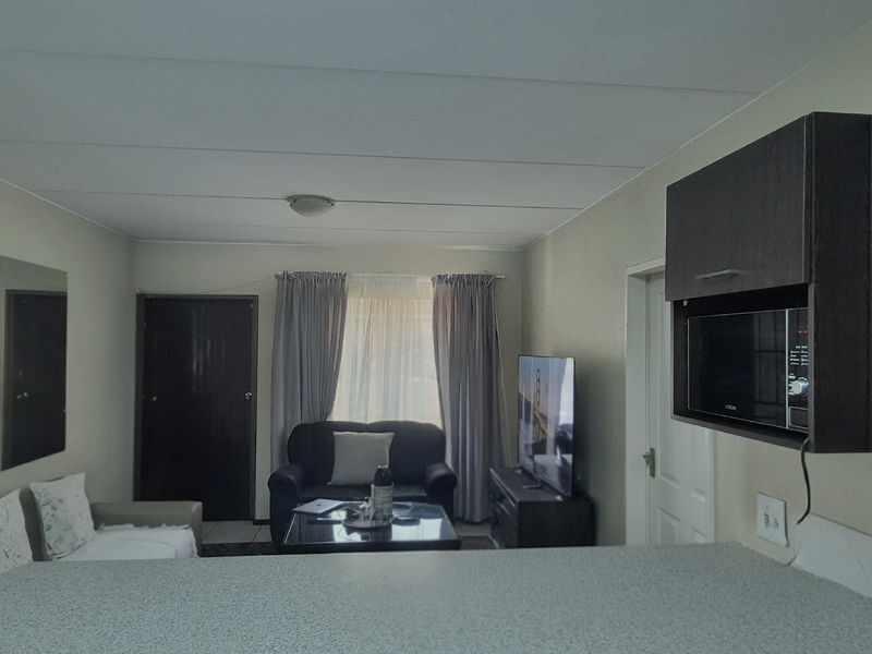 Open-plan living area featuring a compact kitchen with built-in cabinetry and microwave, flowing into a comfortable lounge space.