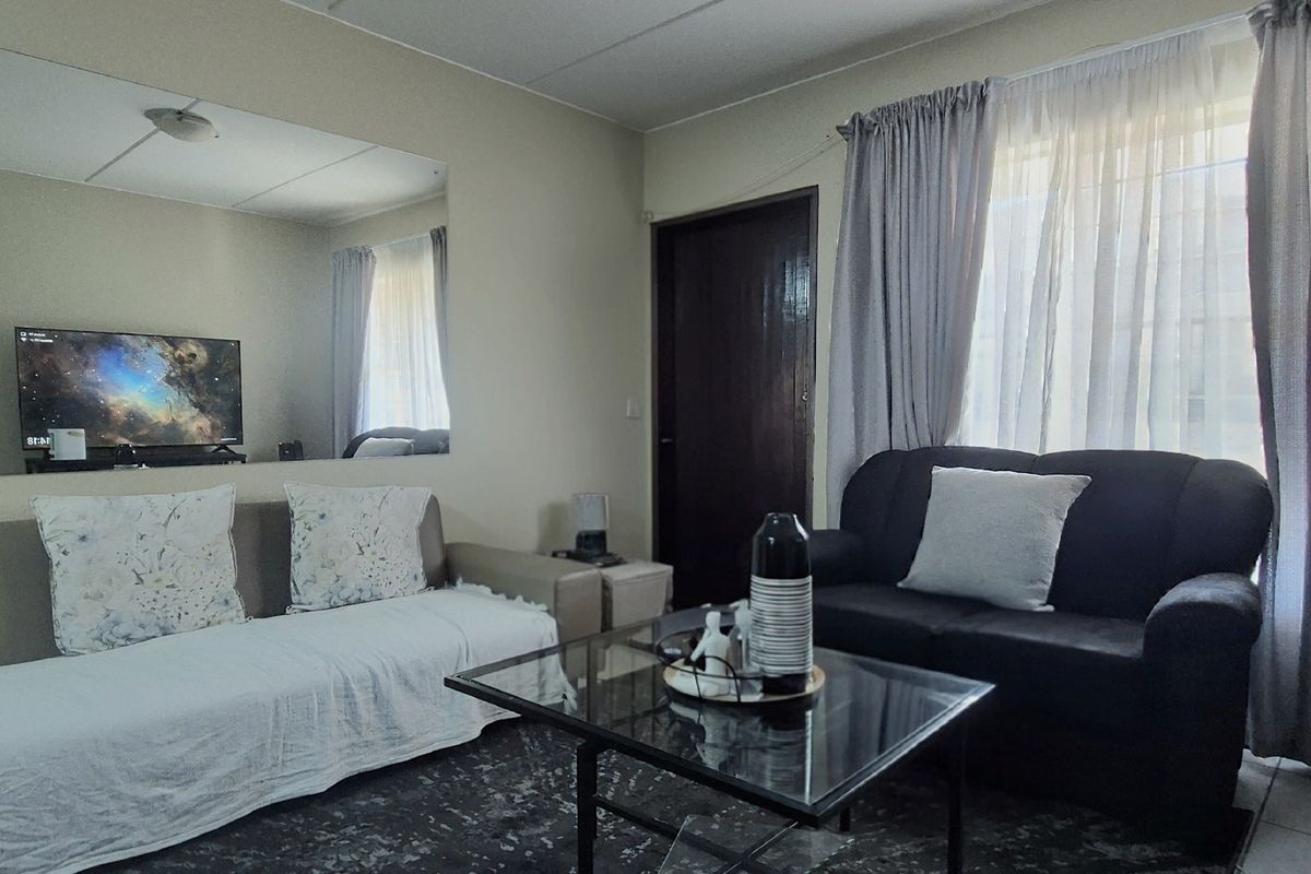 A living room featuring tiled flooring, a large wall-mounted mirror, and window treatments, providing a functional space for relaxation.