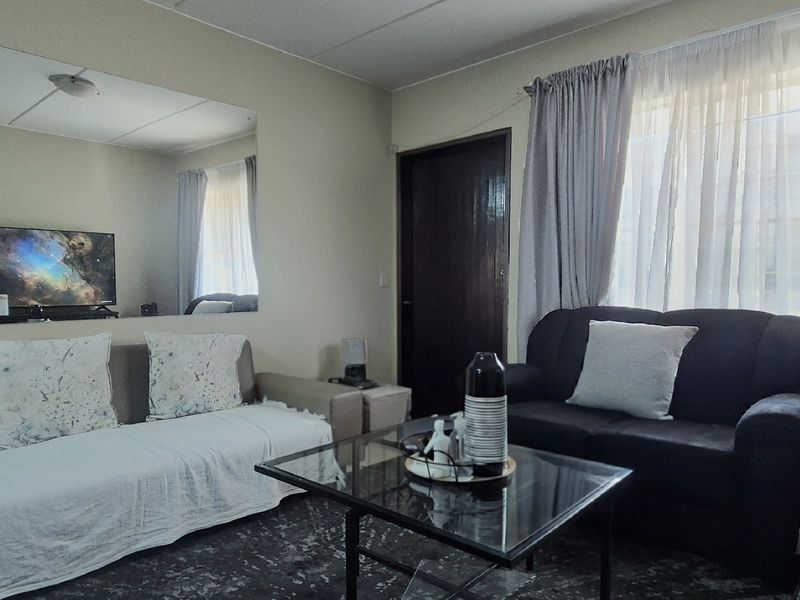 A living room featuring tiled flooring, a large wall-mounted mirror, and window treatments, providing a functional space for relaxation.
