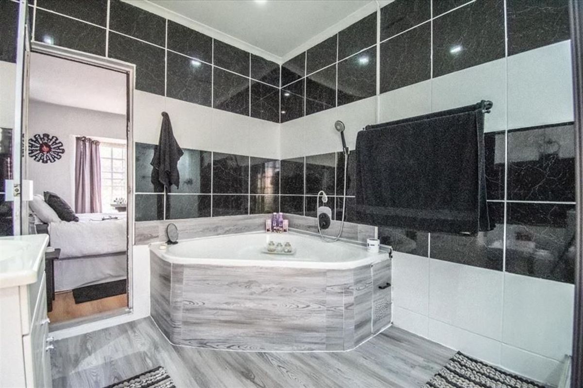 Bathroom featuring a corner bathtub with handheld shower attachment and contrasting black and white wall tiling.
