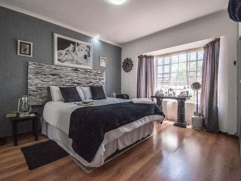 A well-lit bedroom featuring laminate flooring, a prominent bay window, and a decorative accent wall, providing a comfortable and functional living space.