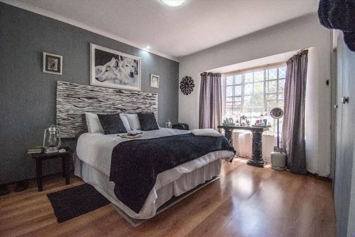 A well-lit bedroom featuring laminate flooring, a prominent bay window, and a decorative accent wall, providing a comfortable and functional living space.