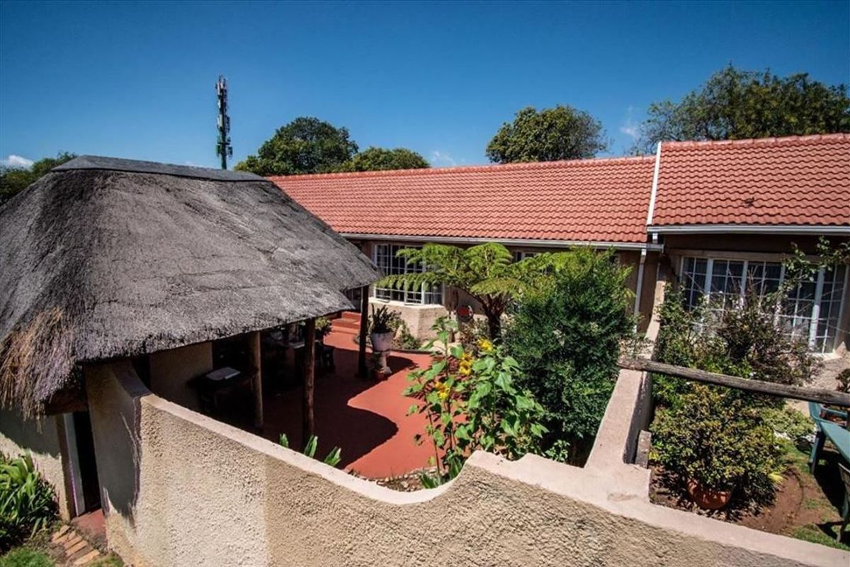 Rear exterior view of the townhouse featuring a thatched lapa, terracotta tiled patio area, and established garden surroundings.