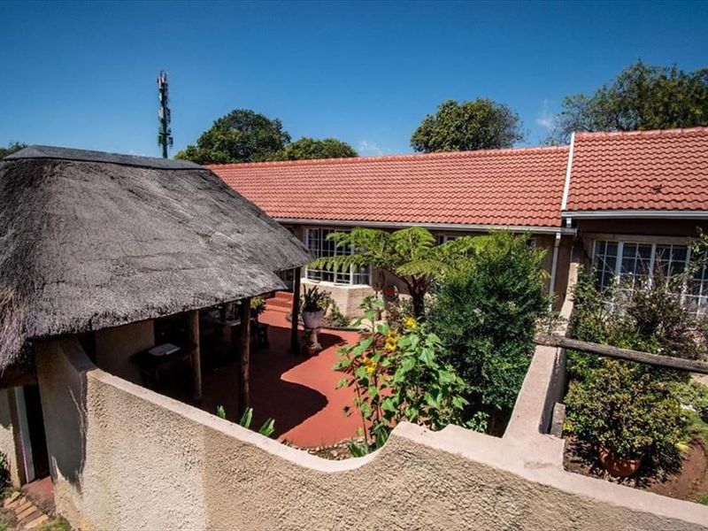 Rear exterior view of the townhouse featuring a thatched lapa, terracotta tiled patio area, and established garden surroundings.