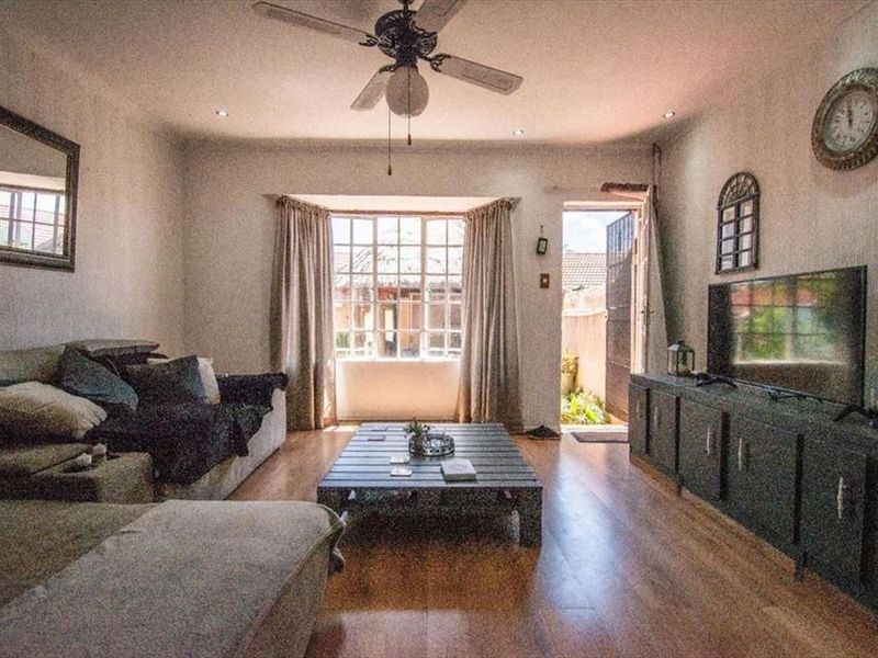 A cozy living room featuring laminate flooring, a ceiling fan, and a bay window with direct access to an outdoor area.