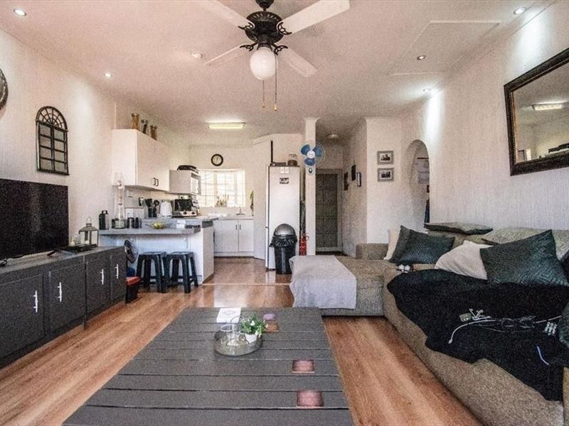 Open-plan living area featuring laminate flooring, recessed lighting, a ceiling fan, and an integrated kitchen space with functional cabinetry.