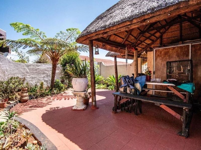 Covered outdoor patio area featuring a traditional thatched roof, timber support structure, and tiled flooring, set within a private walled garden space.