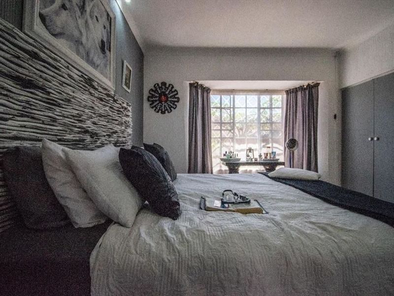 A bedroom featuring a textured feature wall, built-in cupboards, and a bay window that allows natural light into the space.