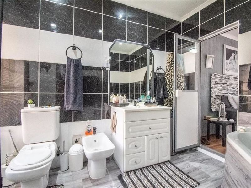 A bathroom featuring black and white wall tiling, a vanity cabinet with basin, toilet, bidet, and a separate shower enclosure.