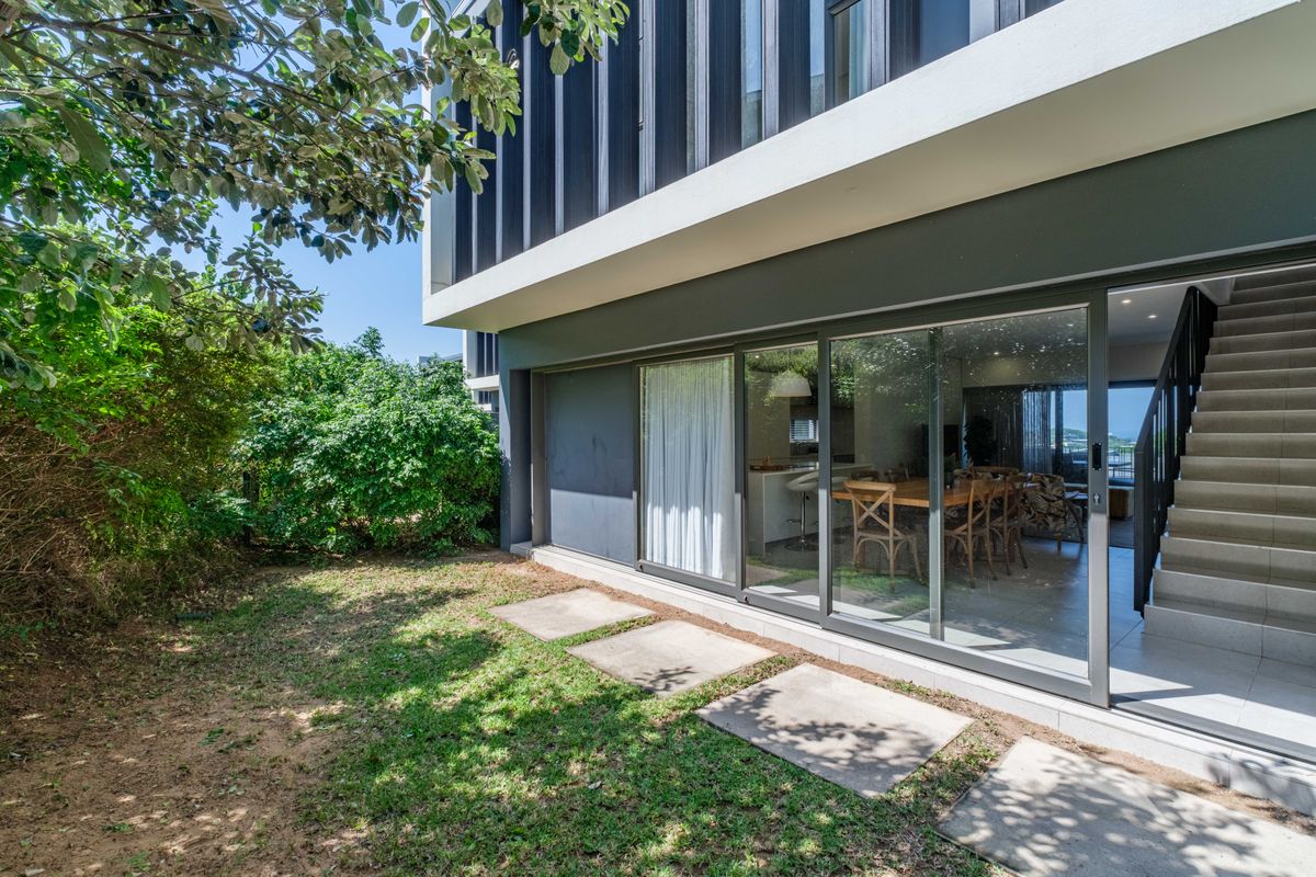 Rear view of the townhouse featuring a small garden, concrete stepping stones, and large sliding glass doors providing access to the interior living space.