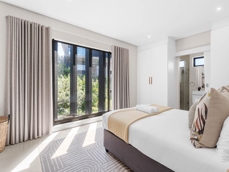 Bright and modern bedroom featuring built-in cupboards, large windows with natural light, and direct access to an en-suite bathroom.