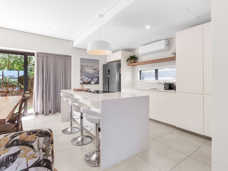 Modern open-plan kitchen featuring a central island with cooktop, sleek cabinetry, and seamless flow to the outdoor area through large sliding glass doors.