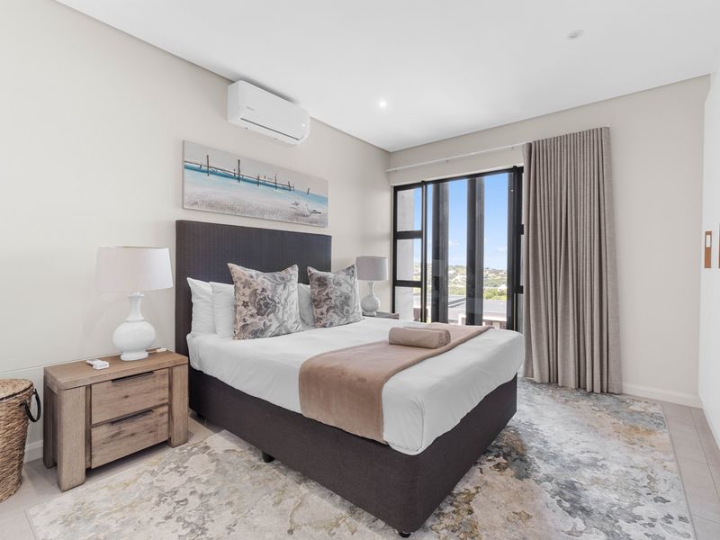 A well-maintained bedroom featuring neutral finishes, a split-system air conditioner, recessed lighting, and large windows providing natural light and views.