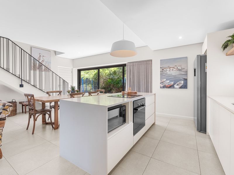 Modern open-plan kitchen and dining area featuring a central island with integrated appliances, tiled flooring, and direct access to the rear garden.