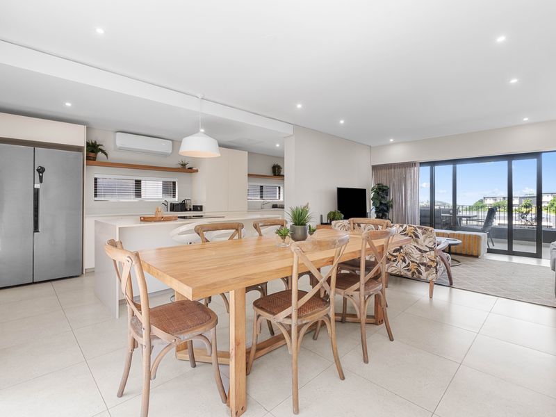 Spacious open-plan living and dining area featuring a modern kitchen with island, tiled floors, and seamless access to an outdoor balcony.