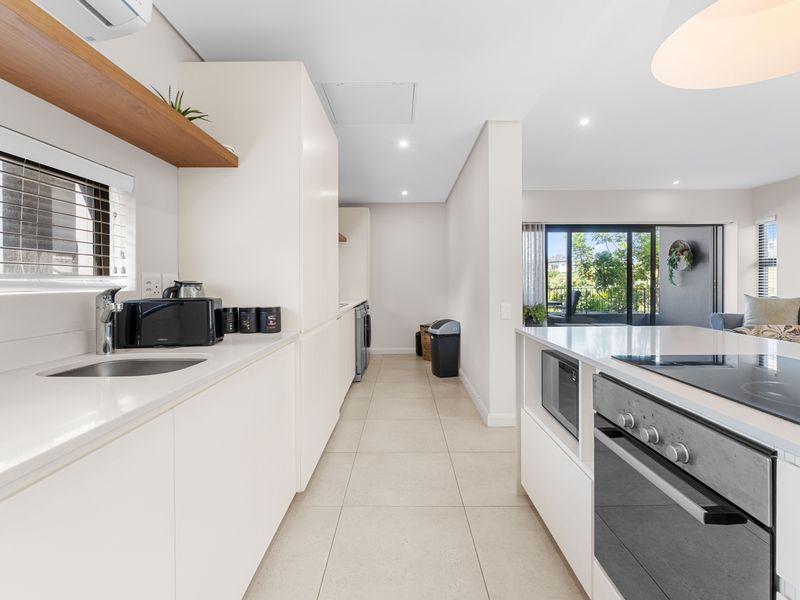 Modern open-plan kitchen featuring sleek white cabinetry, stone countertops, integrated appliances, and seamless flow to the outdoor patio area.