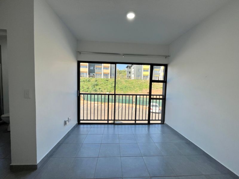 An empty, well-lit living area featuring neutral tiled flooring and a large sliding glass door leading to a balcony with exterior views.