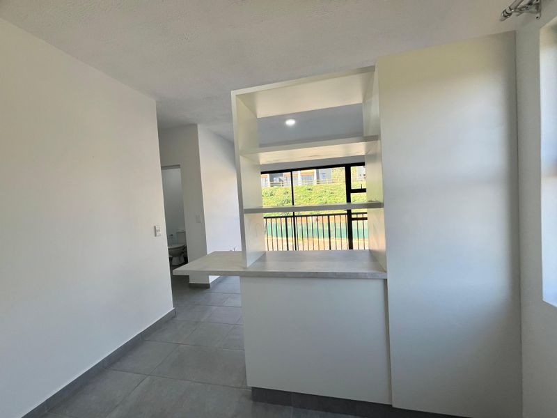 An open-plan living area featuring modern tiled flooring, a built-in breakfast bar with integrated shelving, and access to a balcony.