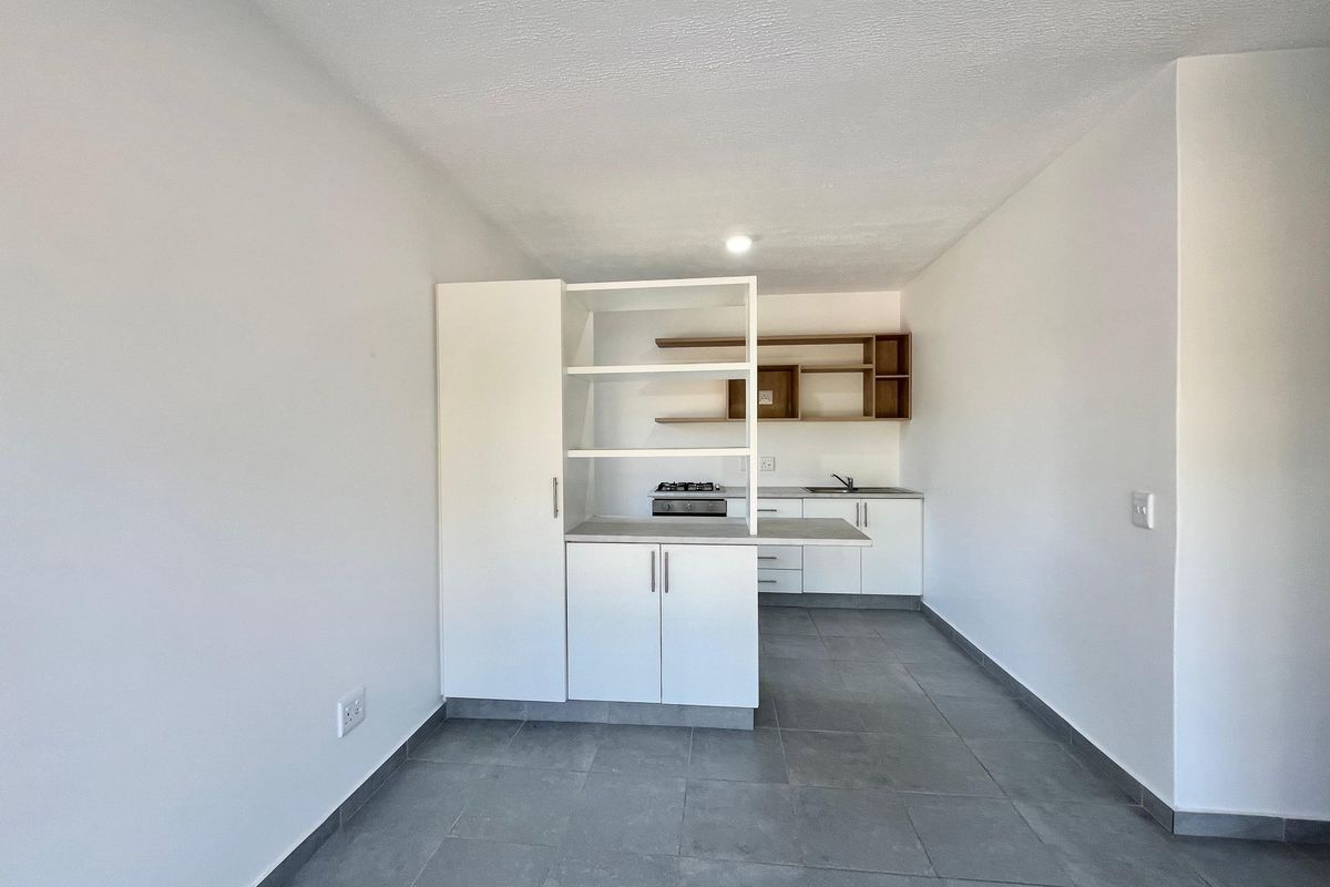 Modern open-plan kitchen featuring white cabinetry, gas hob, stainless steel sink, and neutral tiled flooring in a clean, minimalist space.