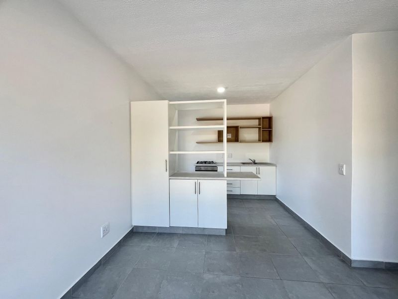 Modern open-plan kitchen featuring white cabinetry, gas hob, stainless steel sink, and neutral tiled flooring in a clean, minimalist space.
