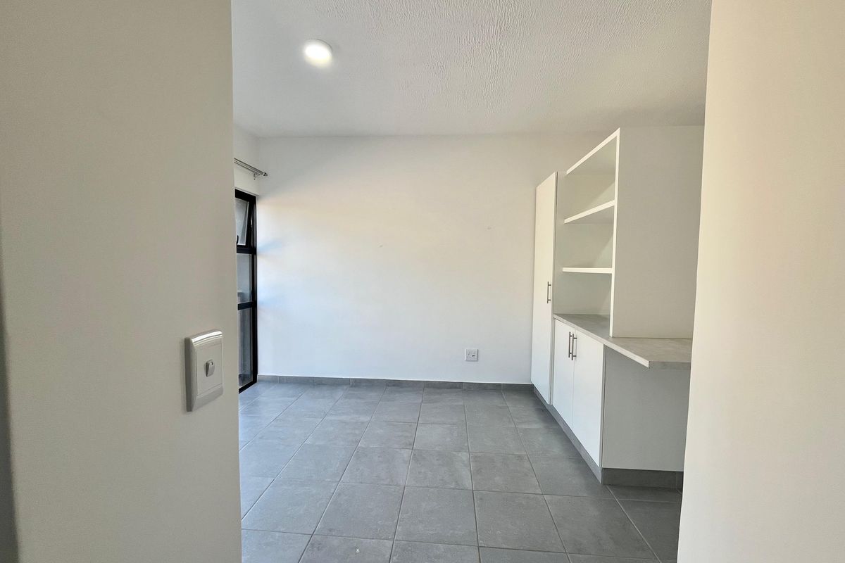 A clean, empty scullery area featuring built-in white cabinetry, open shelving, and modern grey tiled flooring with natural light.