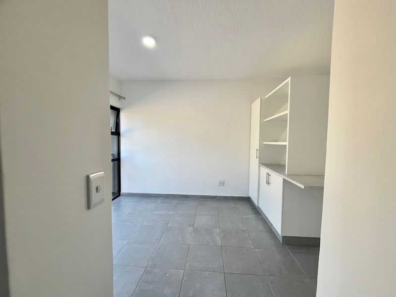 A clean, empty scullery area featuring built-in white cabinetry, open shelving, and modern grey tiled flooring with natural light.