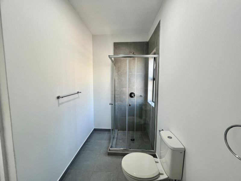 A clean, modern bathroom featuring a glass-enclosed shower with grey tiling, a white toilet, and a wall-mounted towel rail.