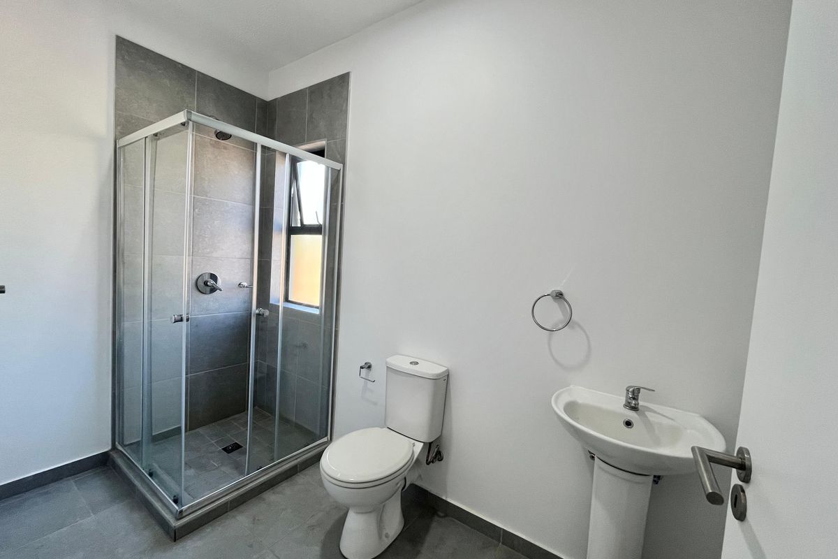 A clean, modern bathroom featuring a glass-enclosed shower, pedestal basin, and toilet with neutral grey floor and wall tiling.