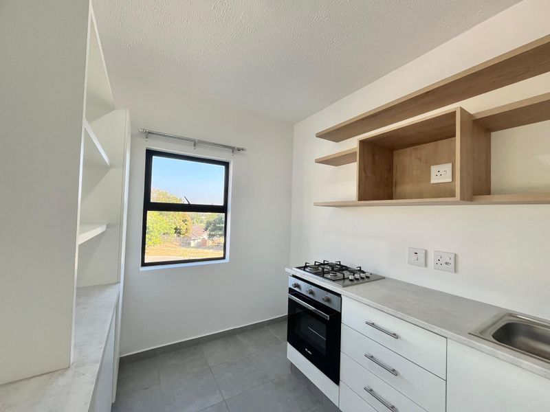 Modern kitchen featuring a gas hob, built-in oven, stainless steel sink, and ample open shelving with clean white cabinetry and tiled flooring.