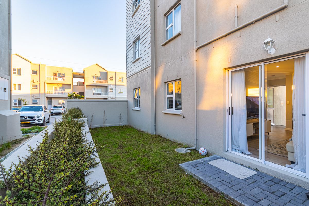 A rear exterior view of the apartment featuring a small private lawn, paved patio area, and sliding glass door access to the living space.