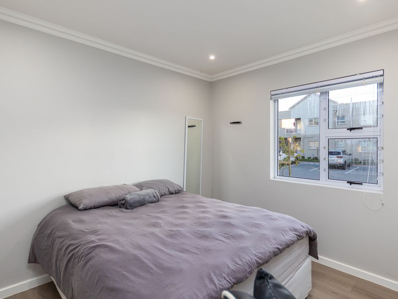 A well-maintained bedroom featuring neutral walls, laminate flooring, recessed downlighting, and a large window providing natural light.