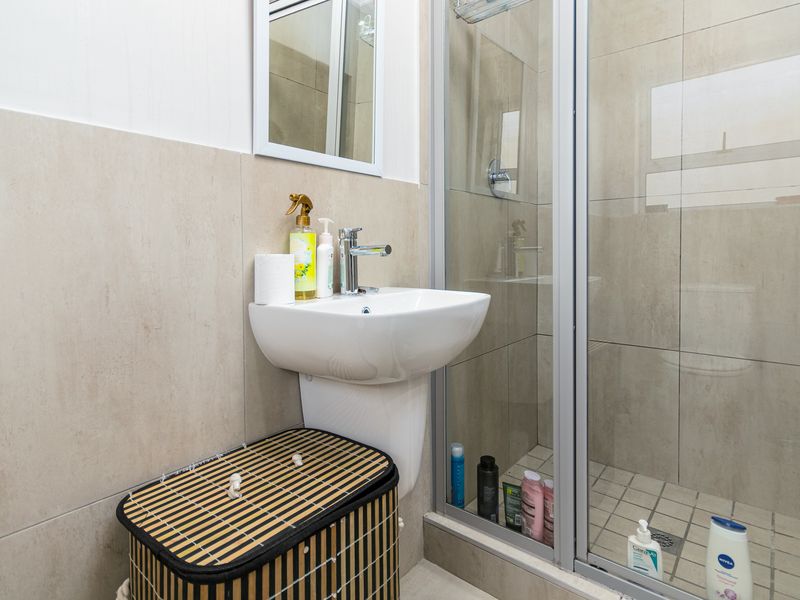A compact bathroom featuring a pedestal basin, modern mixer tap, and a glass-enclosed shower with neutral wall and floor tiling.