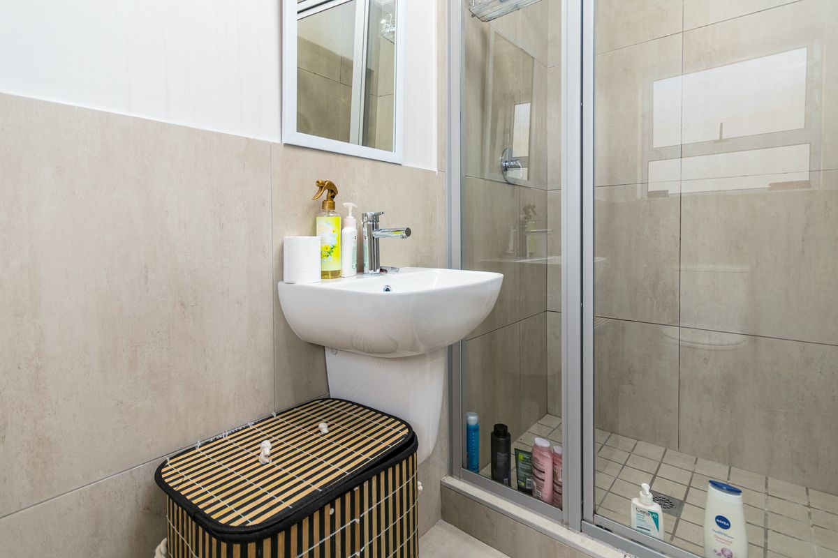 A compact bathroom featuring a pedestal basin, modern mixer tap, and a glass-enclosed shower with neutral wall and floor tiling.