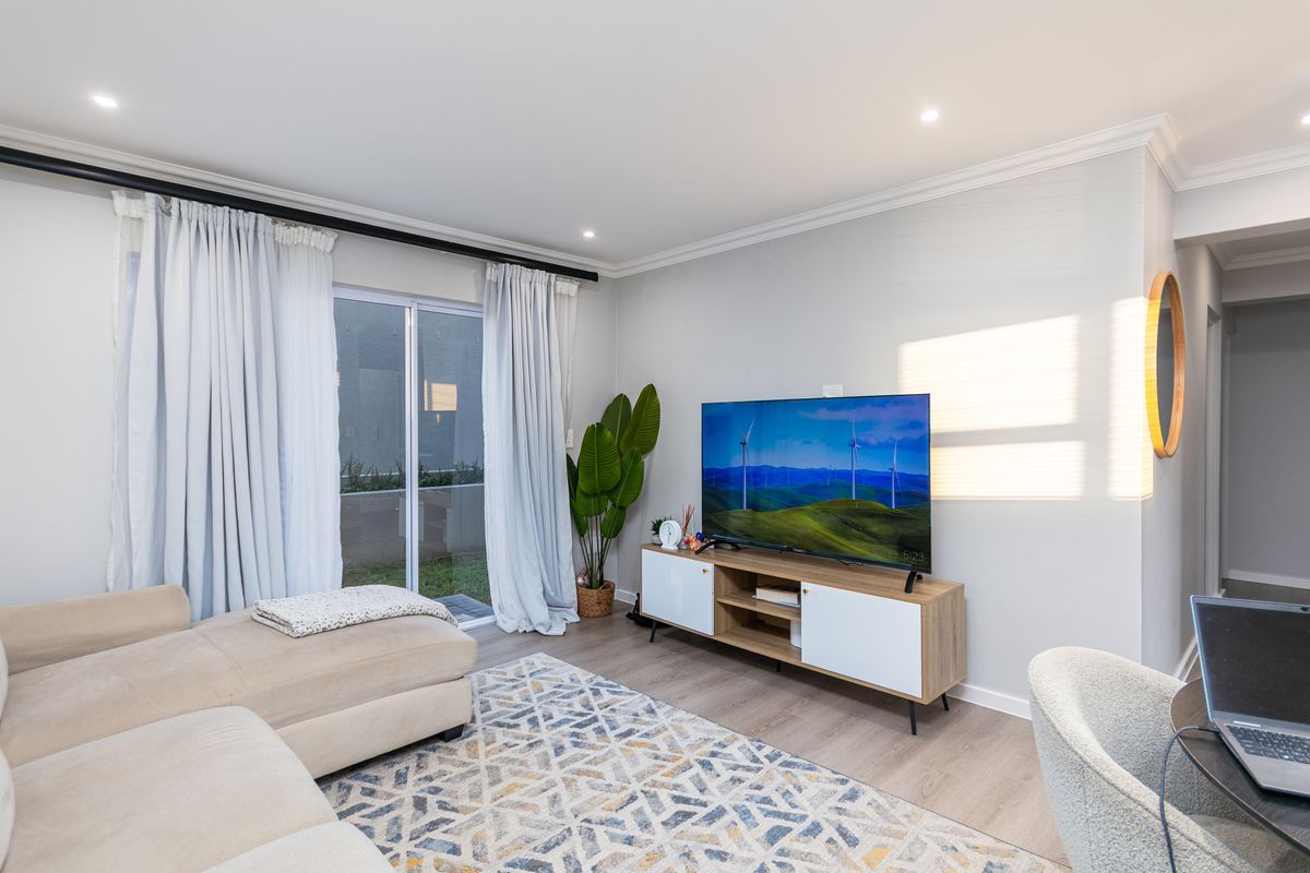 A bright and modern living room featuring laminate flooring, recessed downlights, and a sliding glass door providing access to the outdoor area.