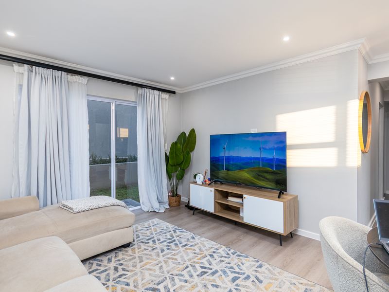A bright and modern living room featuring laminate flooring, recessed downlights, and a sliding glass door providing access to the outdoor area.