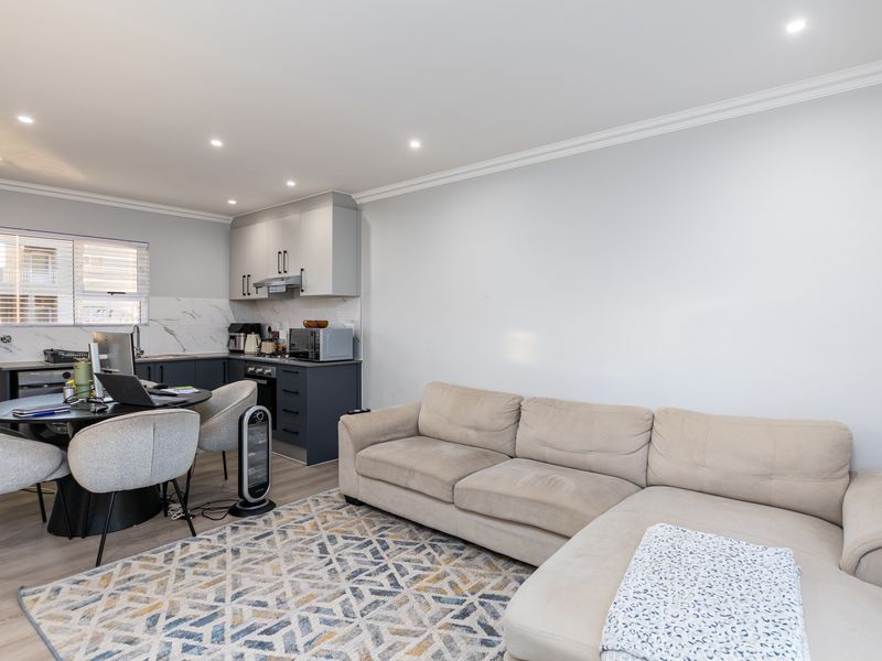 Modern open-plan living area featuring a compact kitchen with built-in cabinetry, integrated appliances, and recessed lighting, seamlessly flowing into the lounge space.