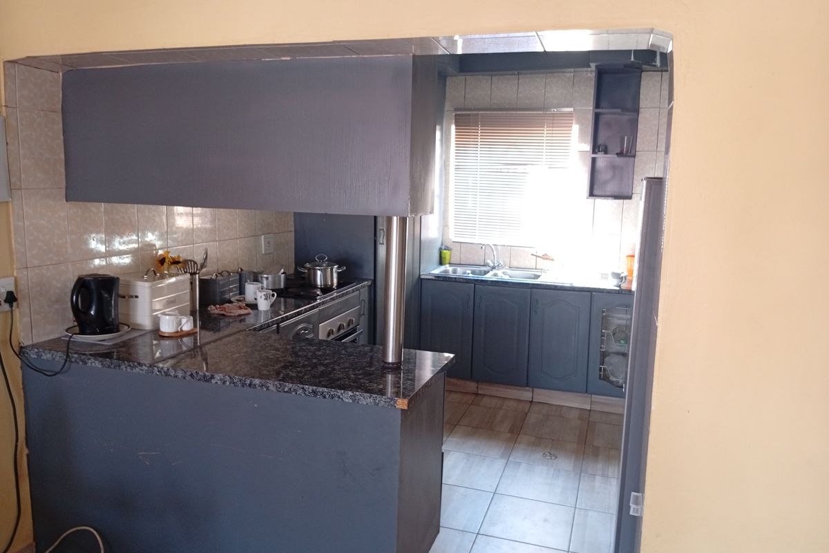 A functional kitchen featuring granite countertops, dark cabinetry, a breakfast bar, and tiled flooring, offering a practical layout with natural light.
