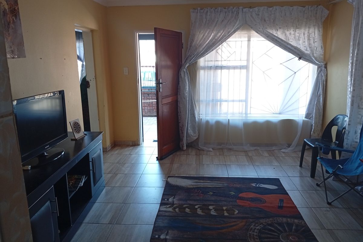A living room featuring tiled flooring, security bars on the windows, and direct access to an exterior area through a wooden door.