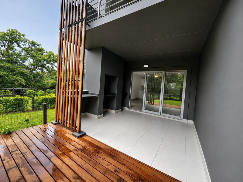 A modern covered patio featuring timber decking, a built-in braai area, and a timber privacy screen, providing seamless access to the interior living space.