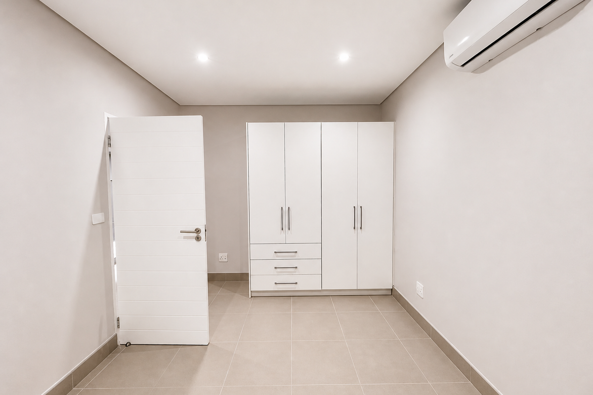 A clean, modern bedroom featuring neutral tiled flooring, built-in cabinetry, and a wall-mounted air conditioning unit.