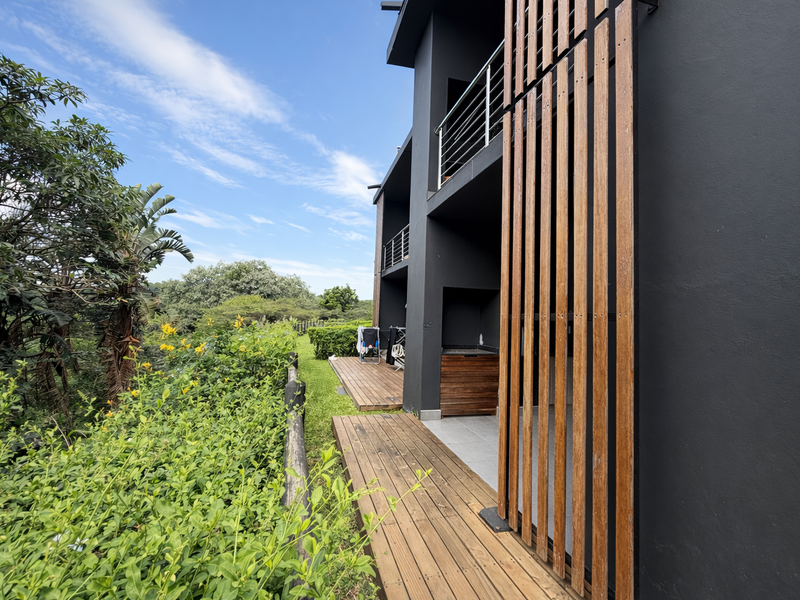 Rear exterior view of the apartment featuring timber decking, a modern vertical wood privacy screen, and a balcony with stainless steel railings.