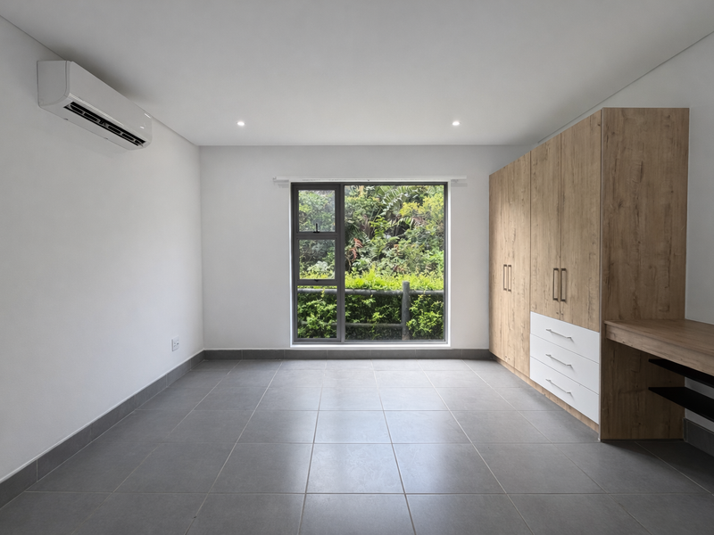 A bright, modern bedroom featuring neutral tiled flooring, a built-in wooden wardrobe with integrated desk, and a split-system air conditioner.