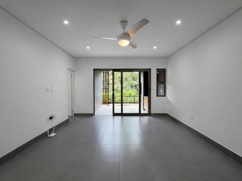 A bright, empty living room featuring neutral tiled flooring, recessed lighting, a ceiling fan, and large sliding glass doors leading to an outdoor area.