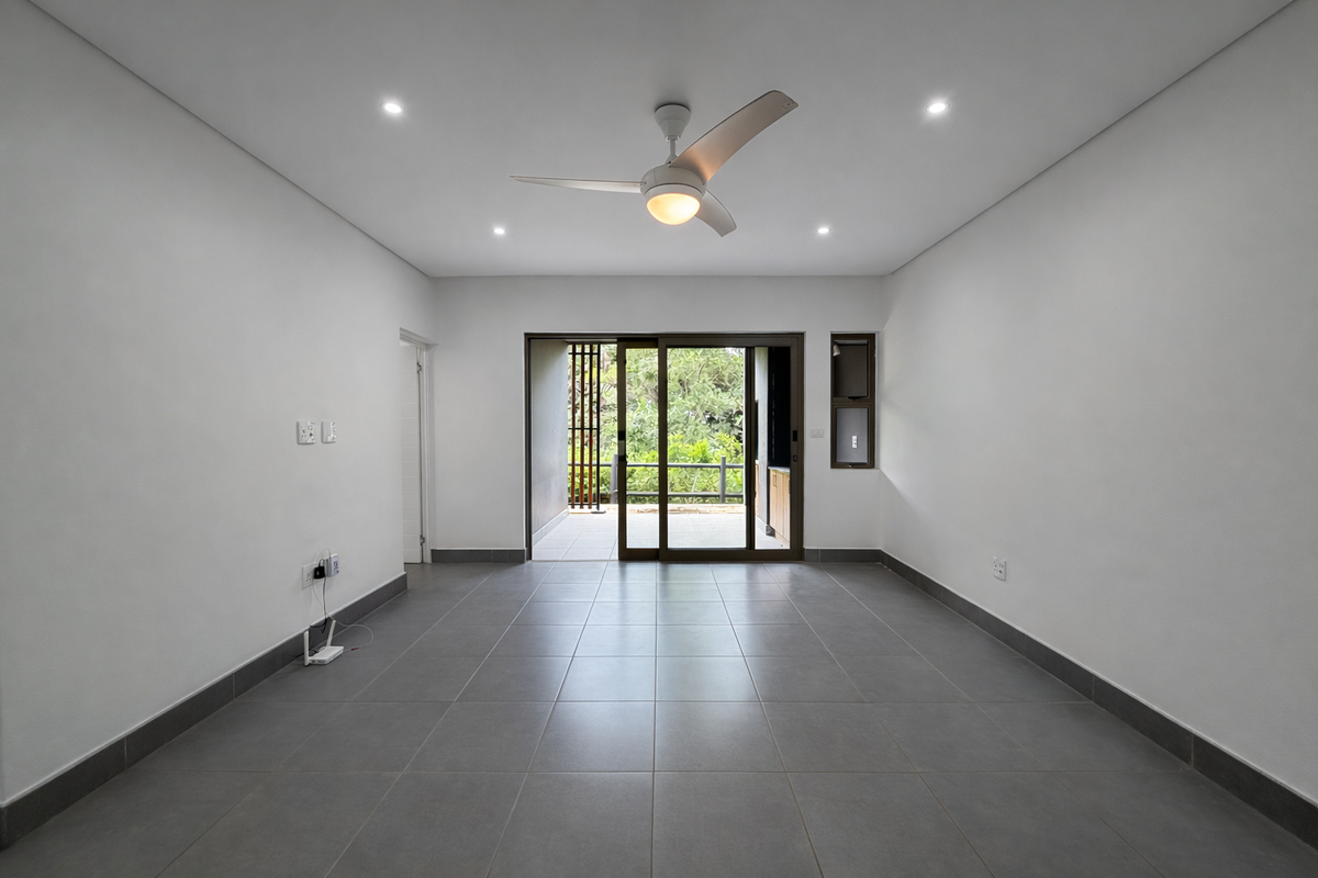 A bright, empty living room featuring neutral tiled flooring, recessed lighting, a ceiling fan, and large sliding glass doors leading to an outdoor area.