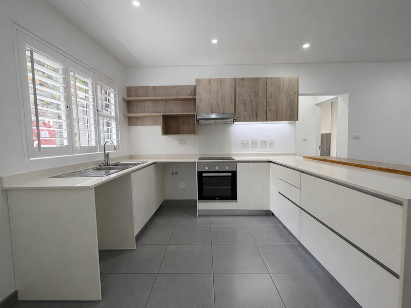 Modern, clean-lined kitchen featuring white cabinetry, wood-tone open shelving, quartz countertops, built-in oven, extractor fan, and neutral tiled flooring.