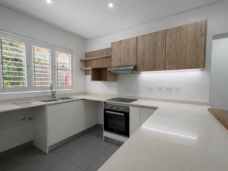 Modern kitchen featuring light wood-tone cabinetry, stone countertops, integrated appliances, and plantation shutters, offering a clean and functional workspace.