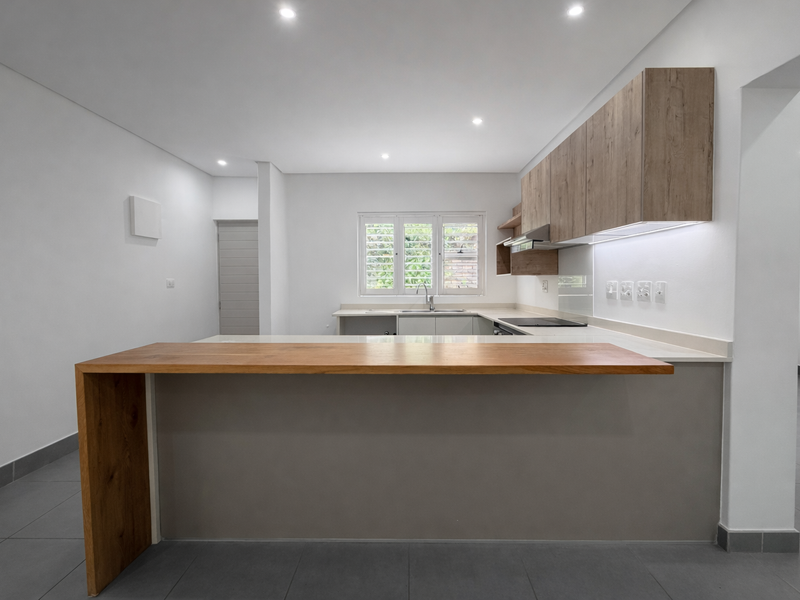 Modern kitchen featuring a wooden breakfast bar, sleek cabinetry, integrated hob, extractor fan, and recessed lighting in a clean, open-plan layout.